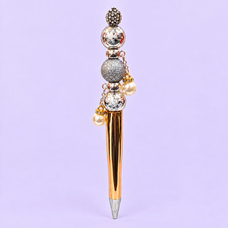 Upright gold pen with silver glitter and patterned ornament beads on a dark lavender background